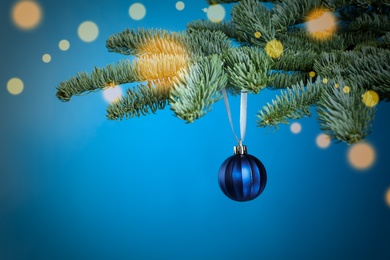 Photo of Beautiful Christmas ball hanging on fir tree branch against light blue background, bokeh effect