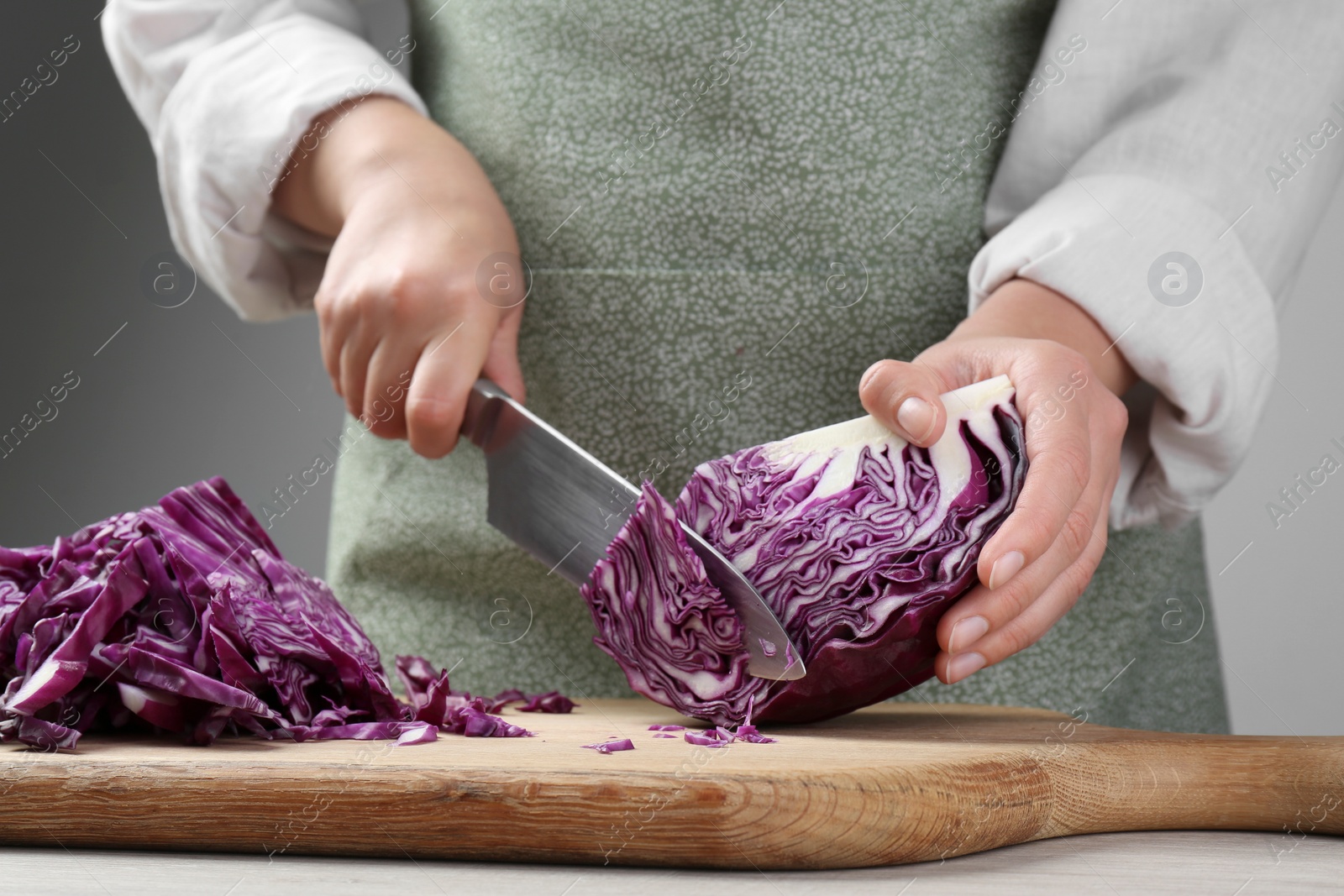 Photo of Woman cutting fresh radicchio cabbage on board at wooden table, closeup