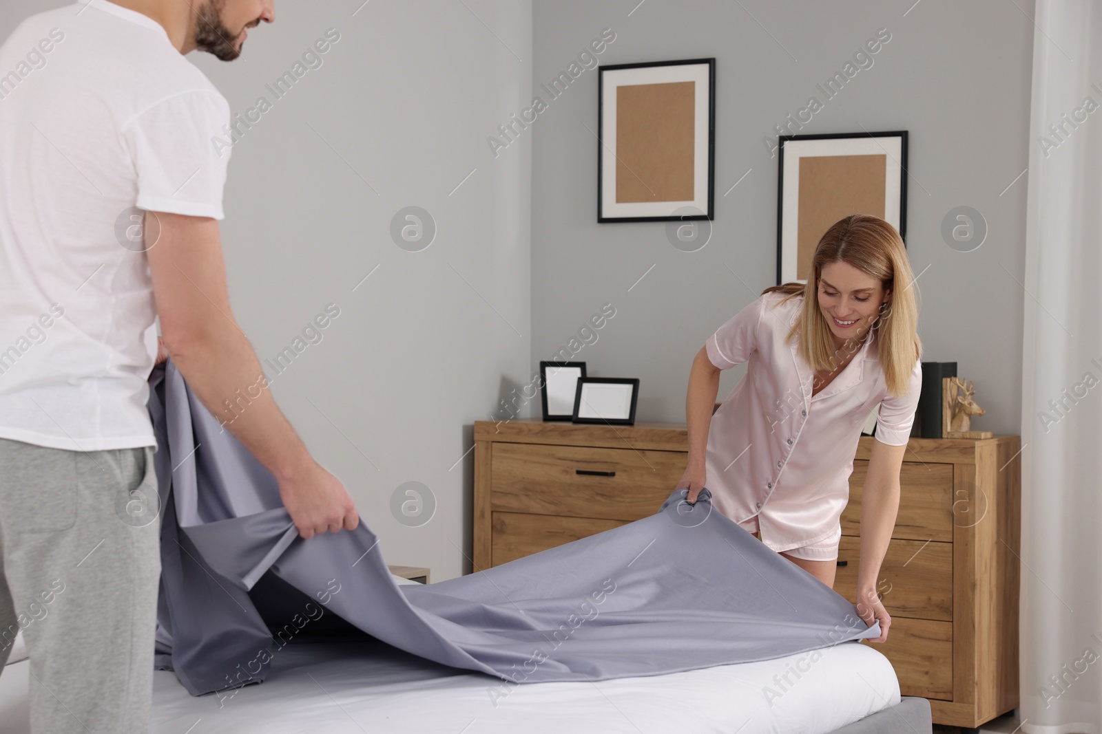 Photo of Couple changing bed linens in room. Domestic chores