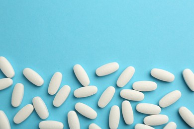 Vitamin pills on light blue background, flat lay. Space for text