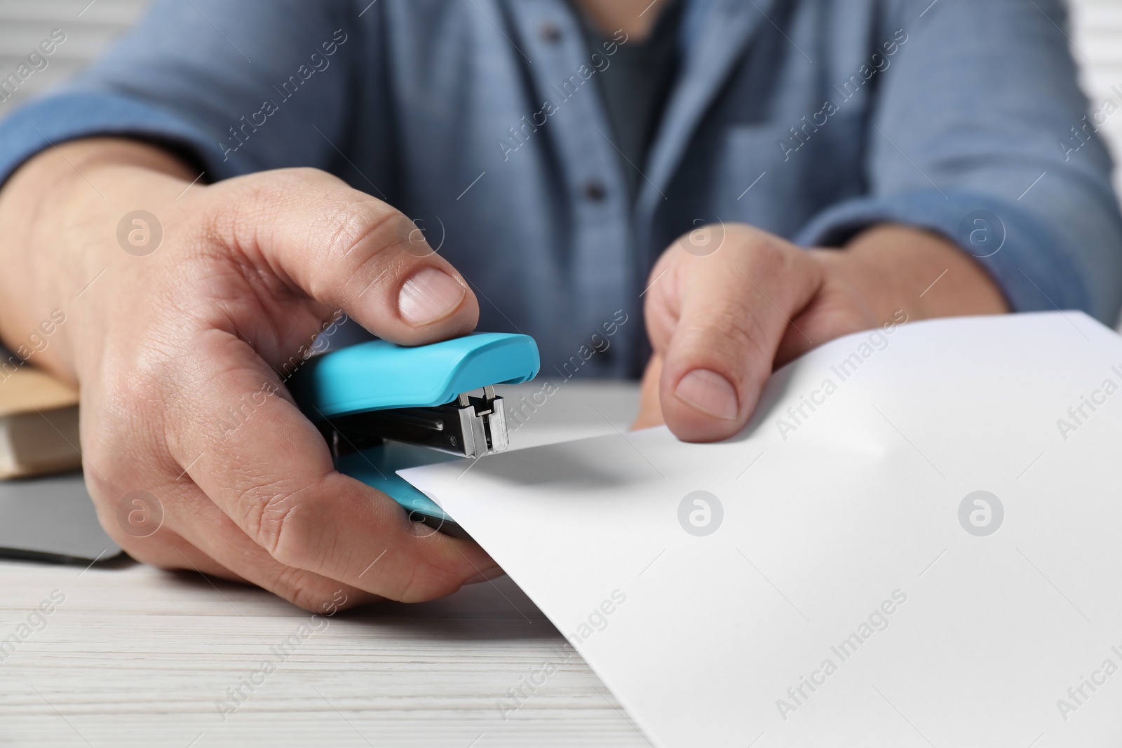 Photo of Man with papers using stapler at white wooden table, closeup