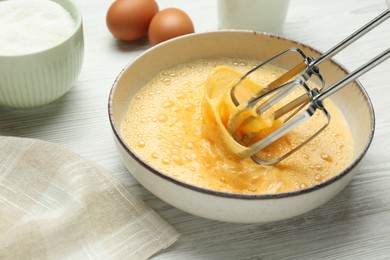 Photo of Beating eggs in bowl with mixer at white wooden table, closeup