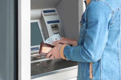 Man with money near cash machine outdoors, closeup