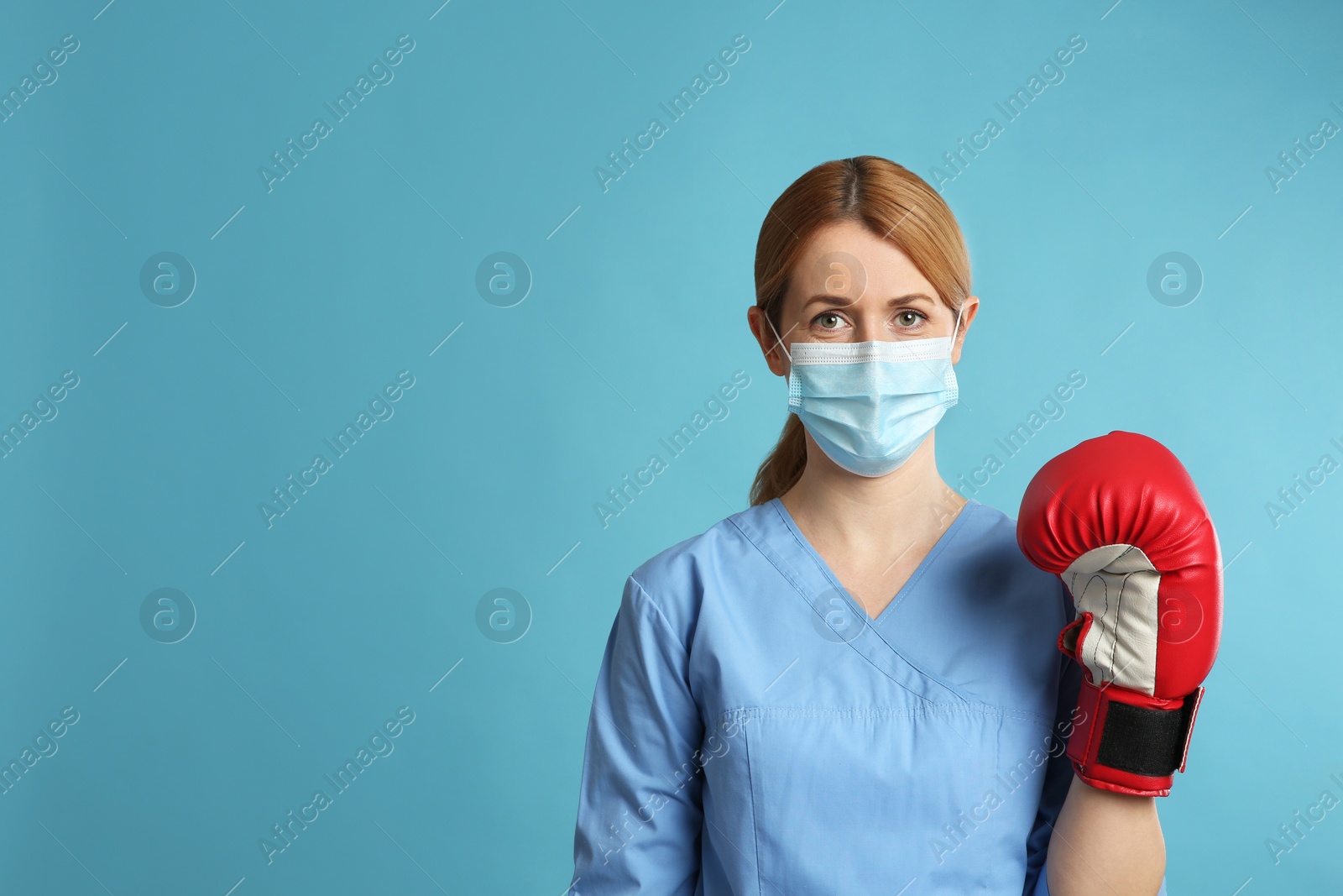 Photo of Doctor with protective mask and boxing gloves on light blue background, space for text. Strong immunity concept