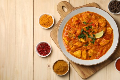 Photo of Delicious chicken curry and spices on wooden table, flat lay. Space for text