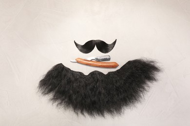 Photo of Artificial moustache, beard and straight razor on light background, flat lay