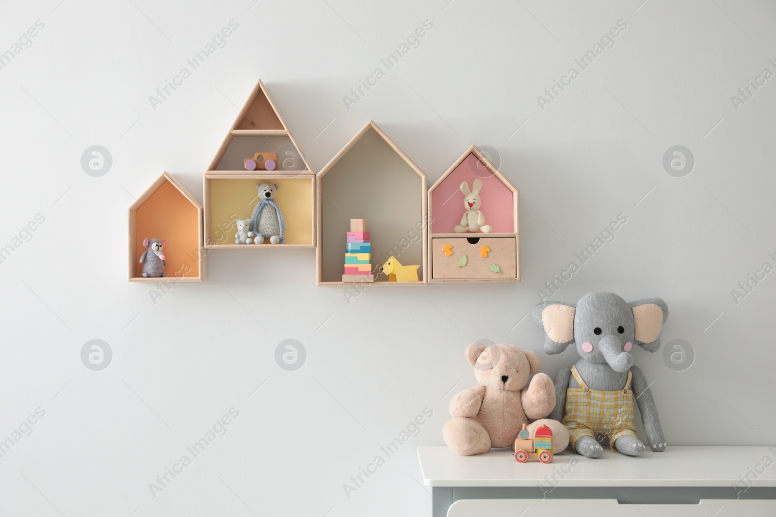 Photo of House shaped shelves and chest of drawers with toys in children's room. Interior design