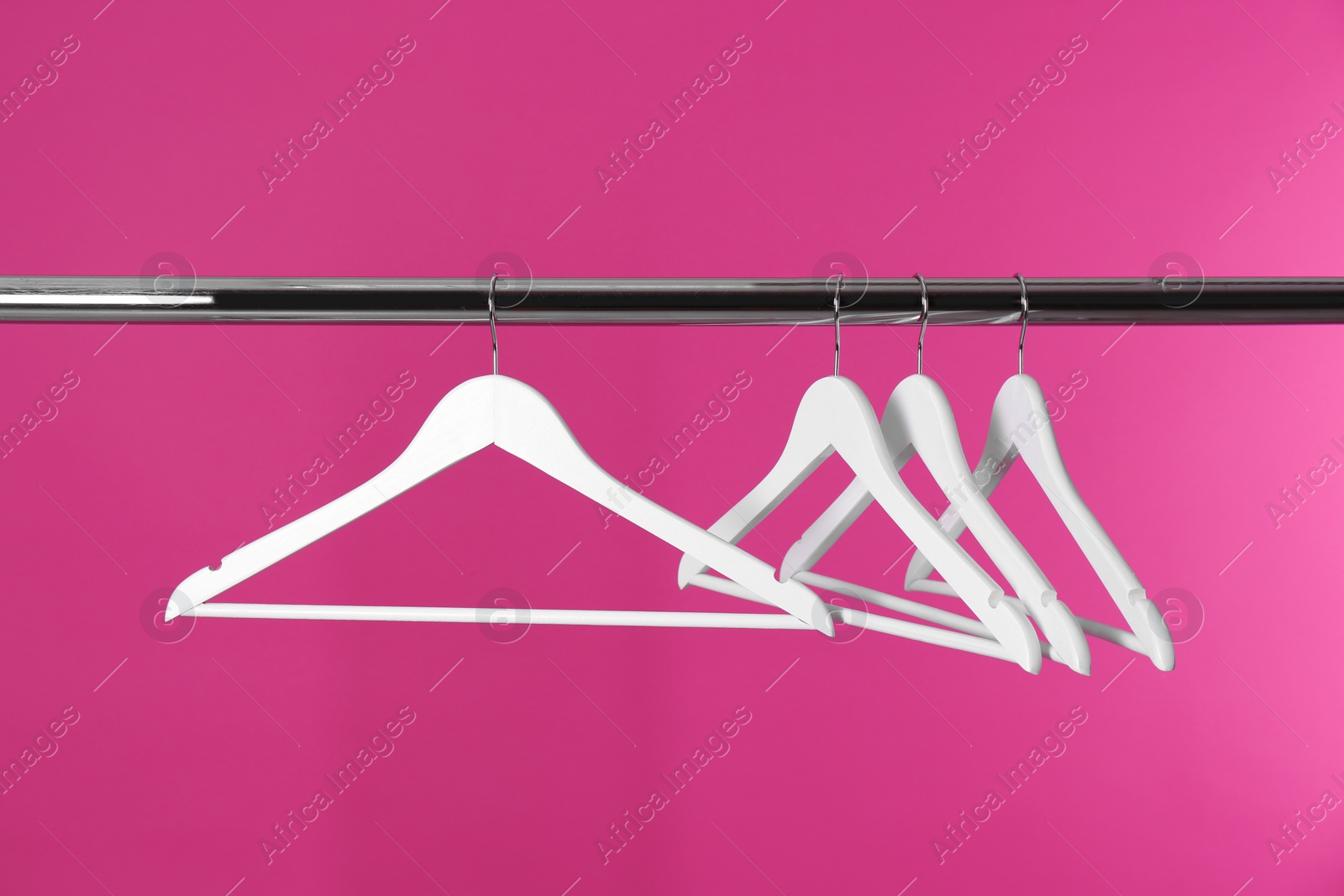 Photo of Metal rack with clothes hangers on color background