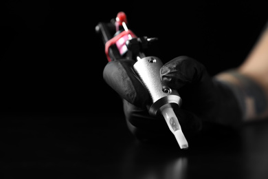 Photo of Tattoo artist with professional machine at table against black background, closeup