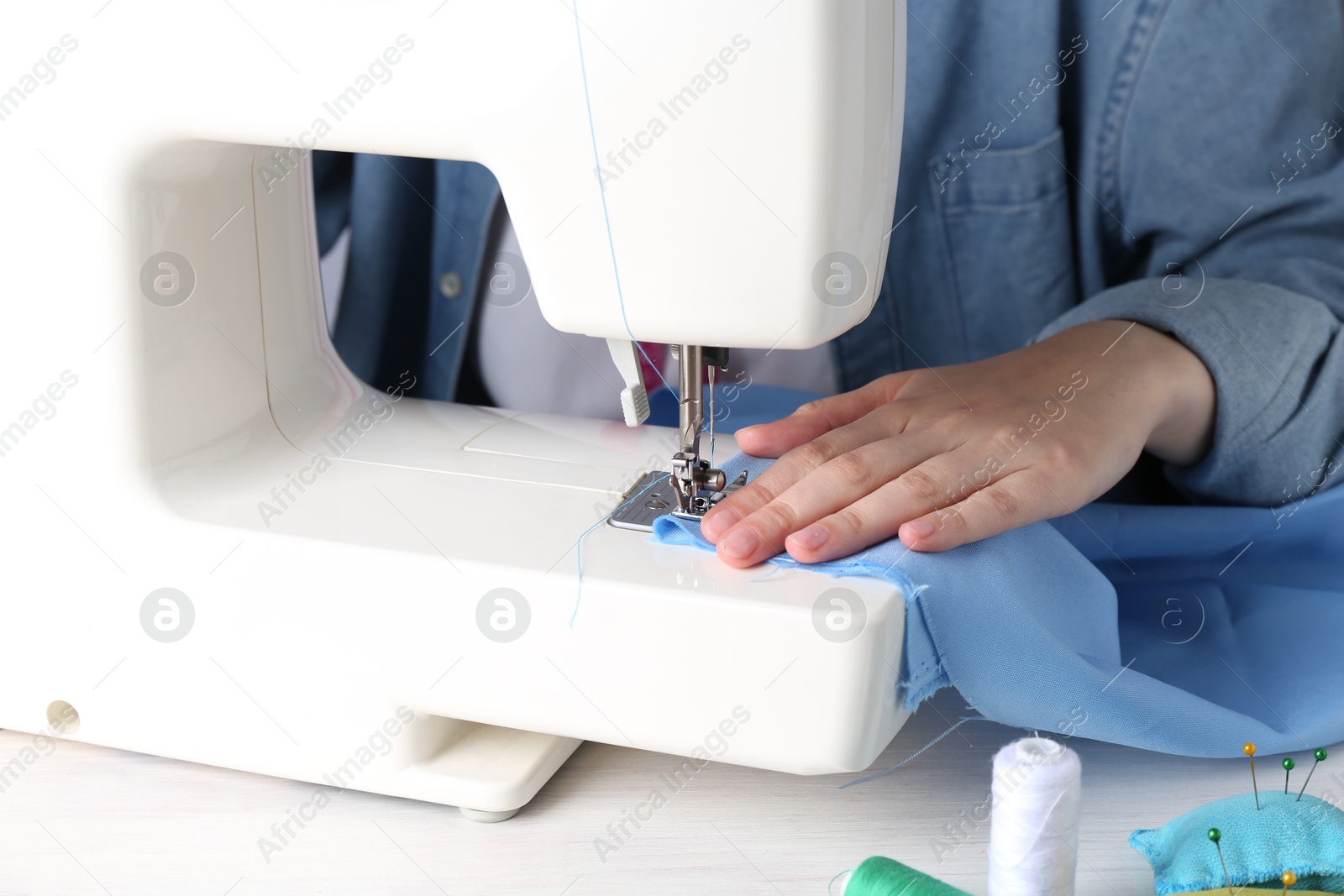 Photo of Seamstress working with sewing machine at white wooden table indoors, closeup