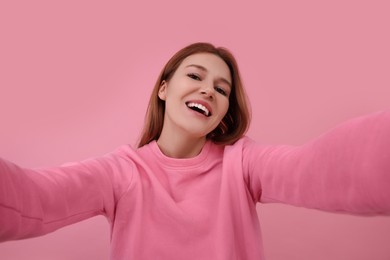 Beautiful woman taking selfie on pink background