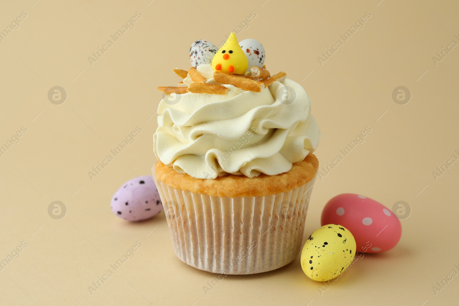 Photo of Tasty Easter cupcake with vanilla cream and candies on beige background