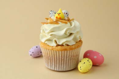 Tasty Easter cupcake with vanilla cream and candies on beige background