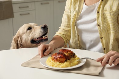 Photo of Cute dog begging for food while owner eating at table, closeup