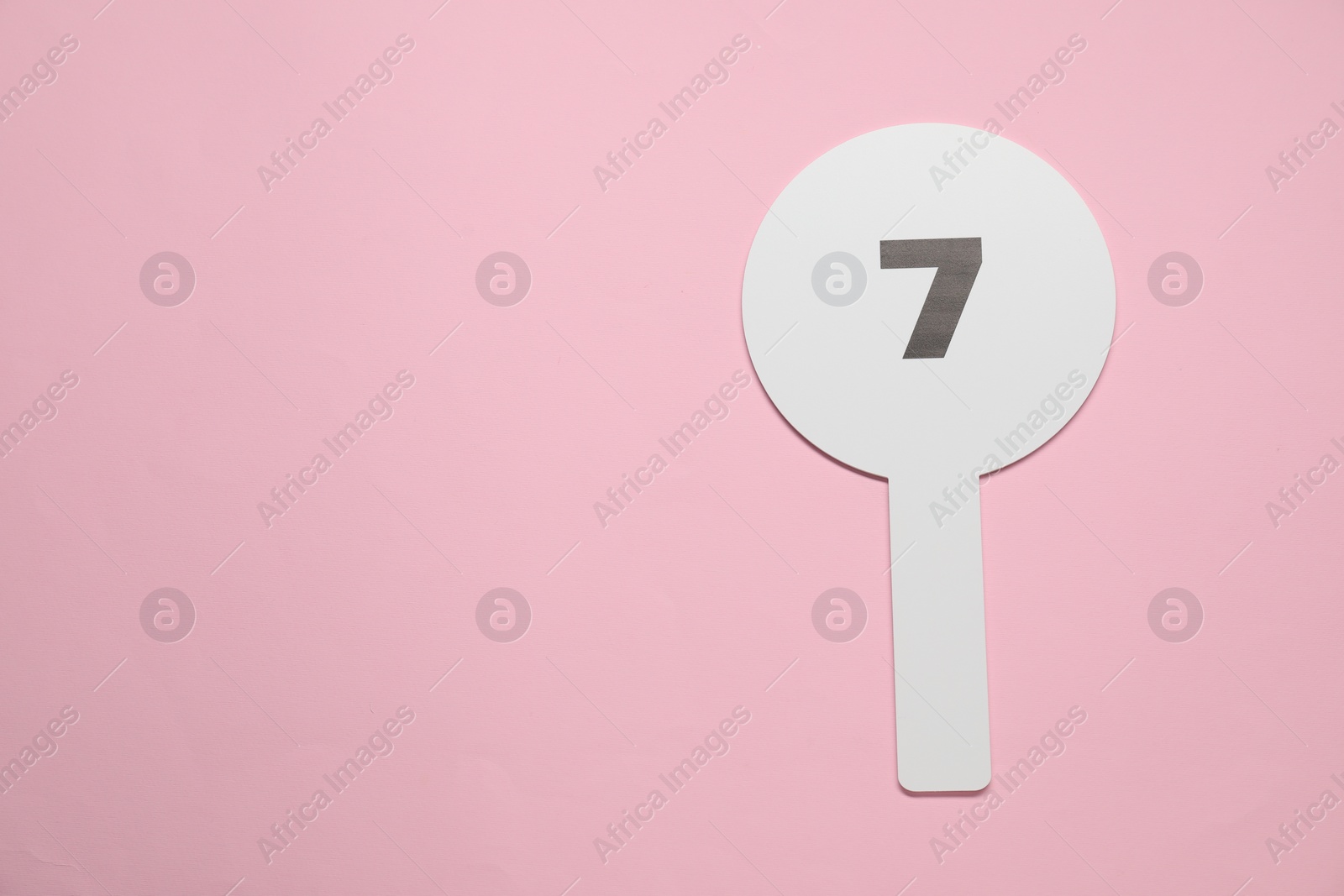 Photo of Auction paddle with number 7 on pink background, top view. Space for text