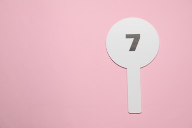 Auction paddle with number 7 on pink background, top view. Space for text