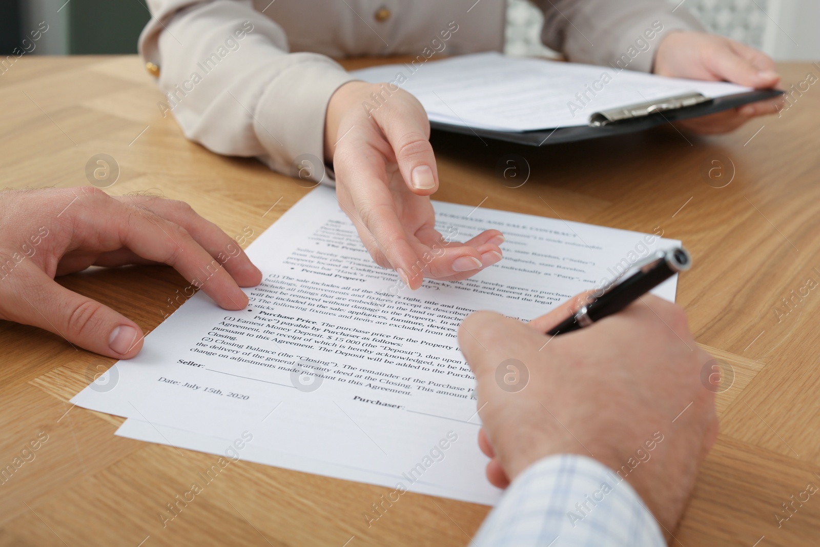 Photo of Businesspeople signing contract at wooden table, closeup of hands