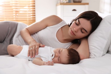 Young mother resting near her sleeping baby on bed at home