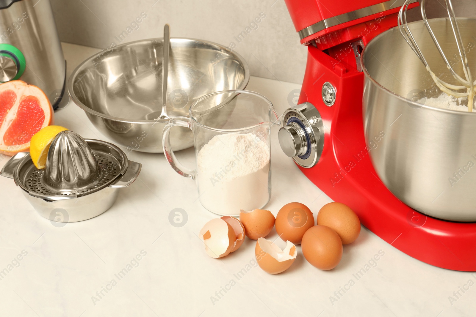 Photo of Modern red stand mixer, different products and squeezer on white marble table