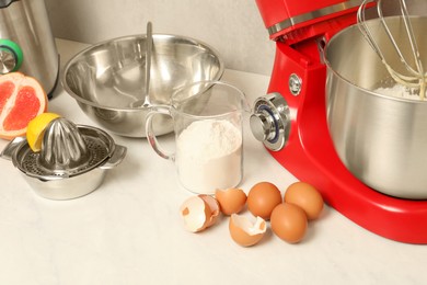 Photo of Modern red stand mixer, different products and squeezer on white marble table