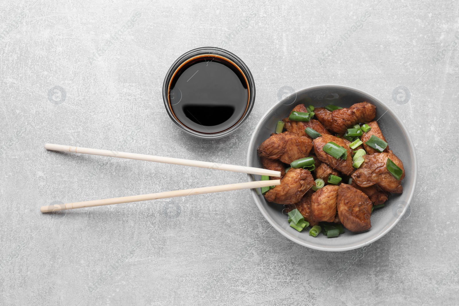 Photo of Tasty soy sauce, chopsticks and roasted meat on grey table, flat lay