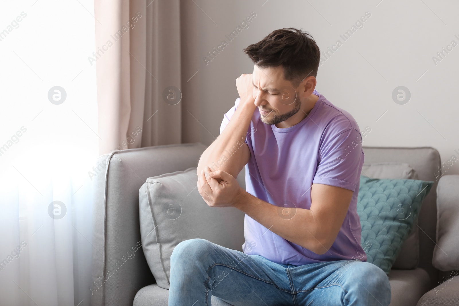 Photo of Young man suffering from elbow pain at home