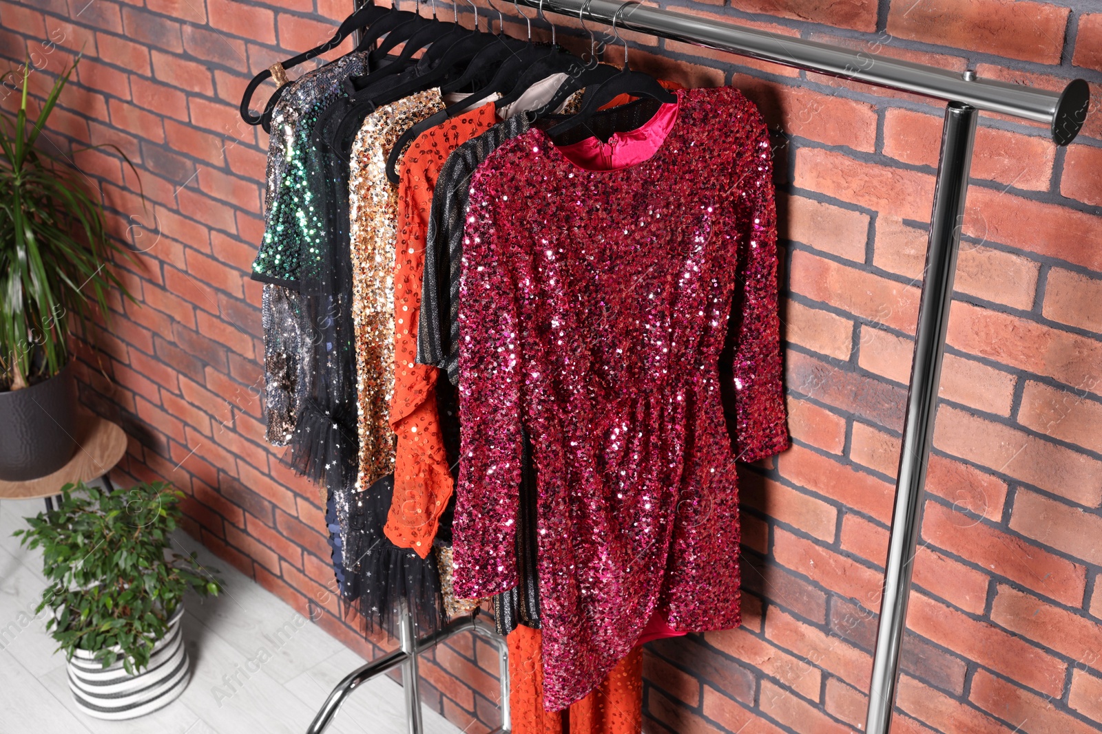 Photo of Rack with collection of fashionable dresses near brick wall in showroom. Preparing for party