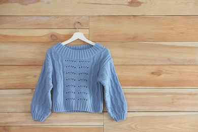Hanger with stylish sweater on wooden wall