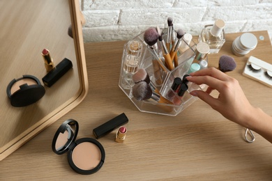 Photo of Woman taking cosmetics from organizer for makeup products on table