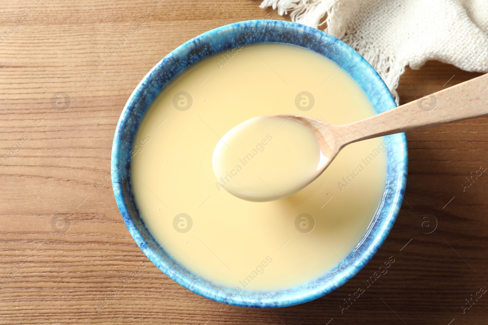 Photo of Spoon and bowl of condensed milk on wooden table, top view. Dairy products