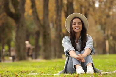 Young woman sitting on green grass in park, space for text