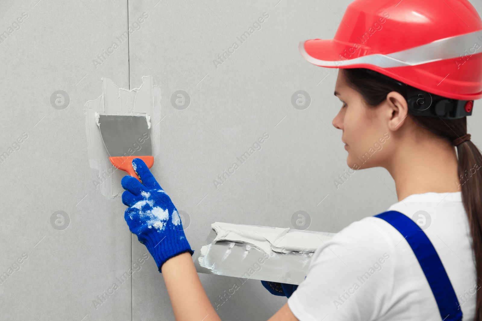 Photo of Professional worker in hard hat plastering wall with putty knives, closeup