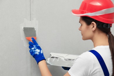 Photo of Professional worker in hard hat plastering wall with putty knives, closeup