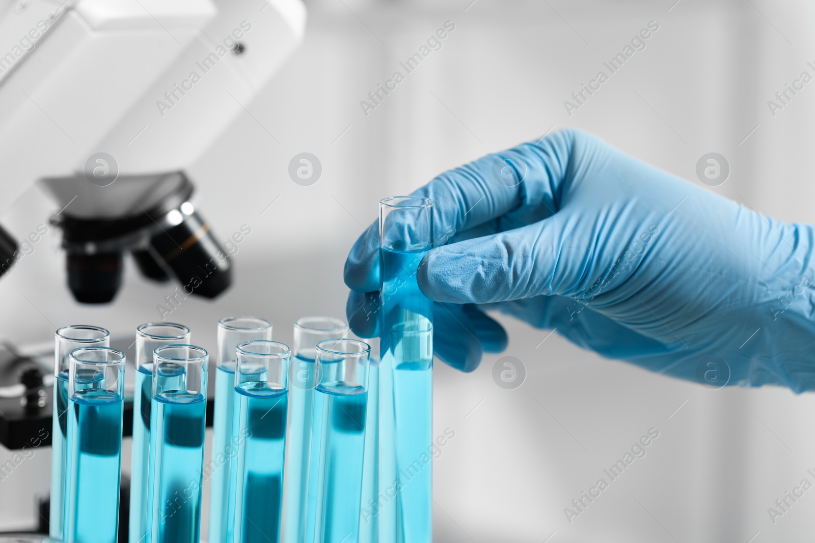 Scientist taking test tube with light blue liquid in laboratory, closeup Photo of Scientist taking test tube with light blue liquid in laboratory, closeup