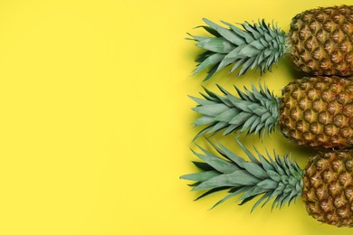 Photo of Whole ripe pineapples on yellow background, flat lay. Space for text