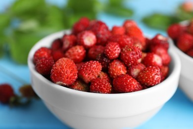 Photo of Fresh wild strawberries in bowl on light blue table, closeup