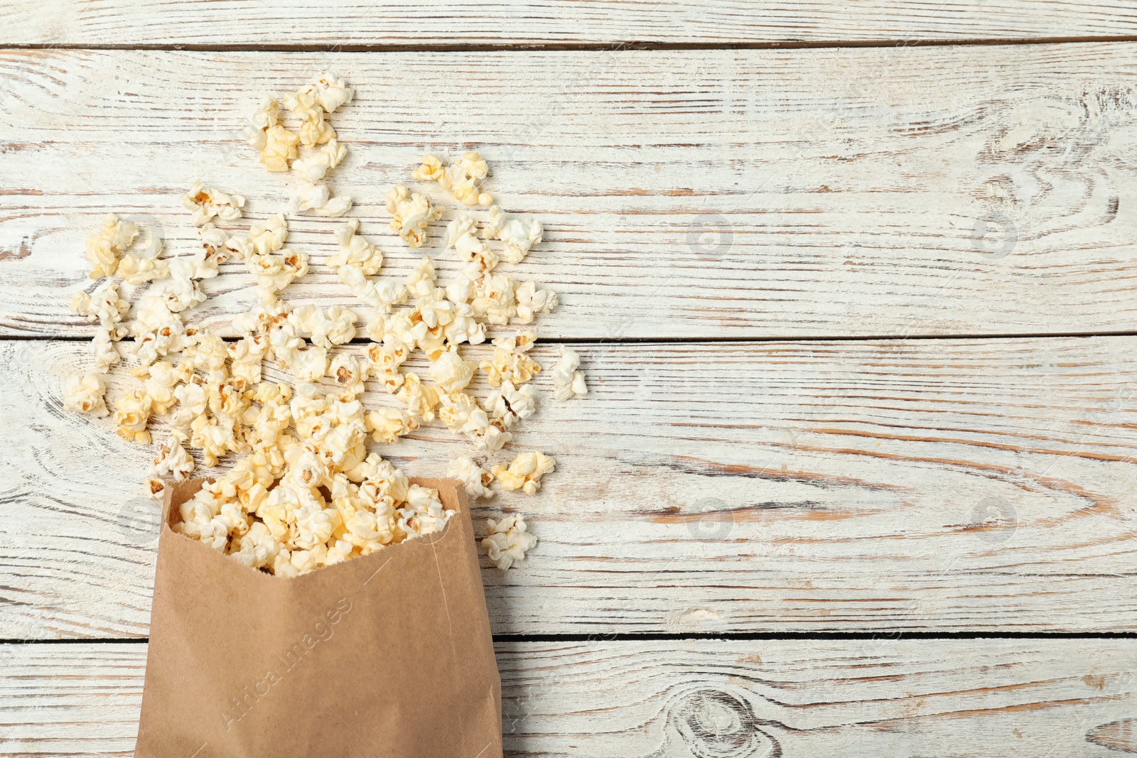 Photo of Overturned paper bag with popcorn on white wooden background, top view. Space for text