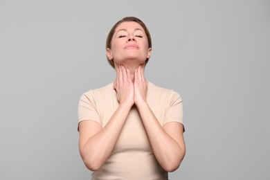 Woman suffering from sore throat on light grey background