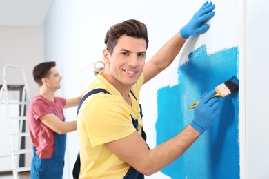 Male decorator painting wall with brush indoors