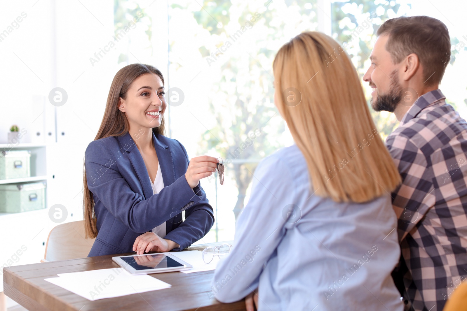 Photo of Female real estate agent giving house key to couple at table in office