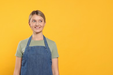 Photo of Beautiful young woman in denim apron on orange background. Space for text