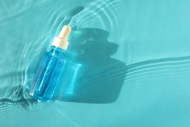 Photo of Bottle of cosmetic serum in water on turquoise background, top view. Space for text