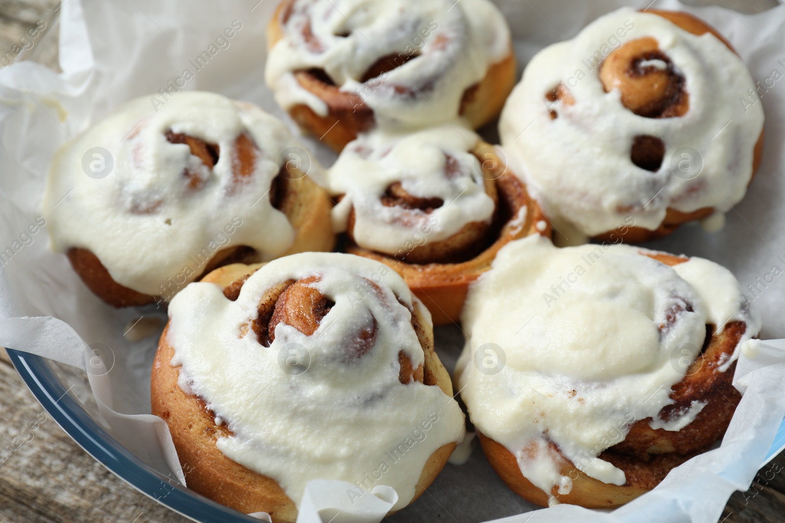 Photo of Many tasty cinnamon rolls with cream in baking dish, closeup