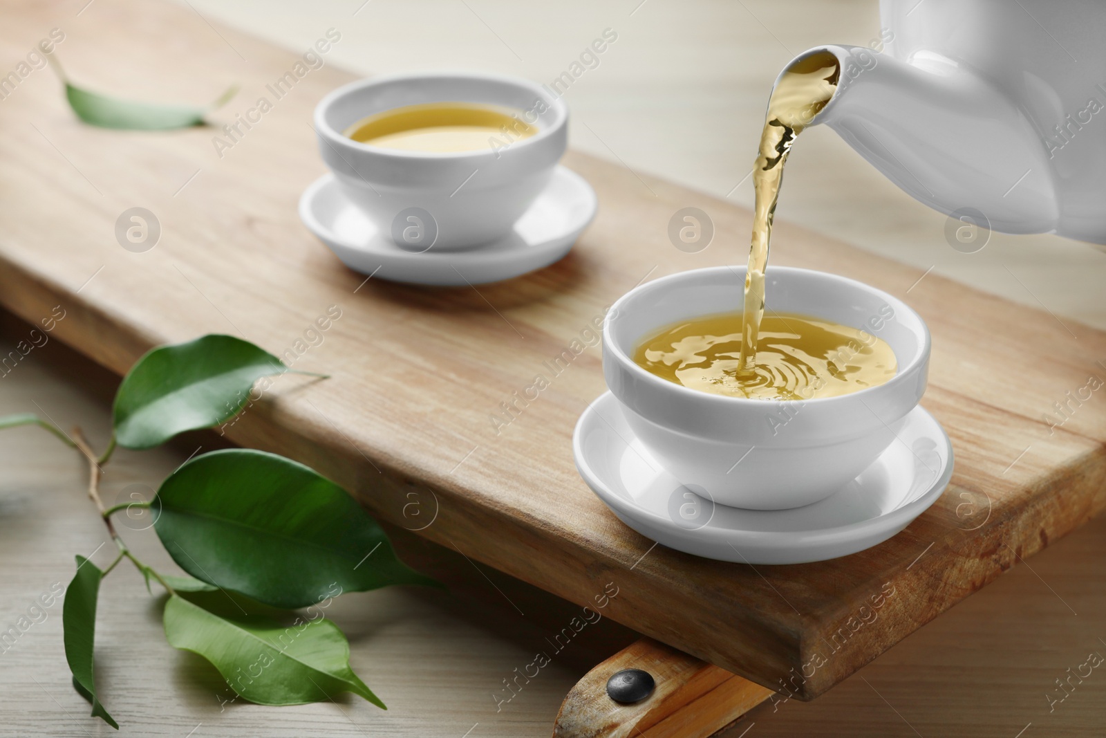 Photo of Pouring green tea into white cup on wooden table, closeup
