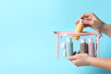 Cosmetic travel kit. Woman putting small bottle with personal care product into plastic bag against light blue background, closeup. Space for text