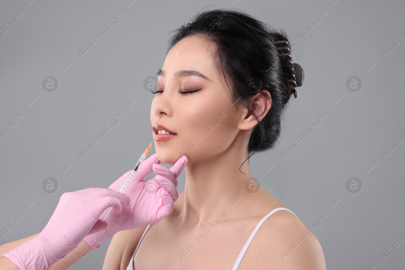Photo of Woman getting lip injection on grey background