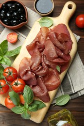 Photo of Board with delicious bresaola and other snacks served on wooden table, flat lay