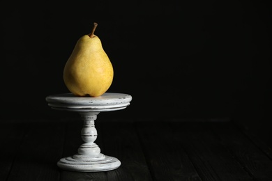 Photo of Stand with fresh ripe pear on table against dark background. Space for text