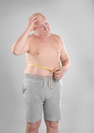 Fat senior man with measuring tape on grey background. Weight loss
