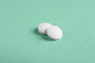 Photo of Two white pills on green background, closeup. Medicinal treatment